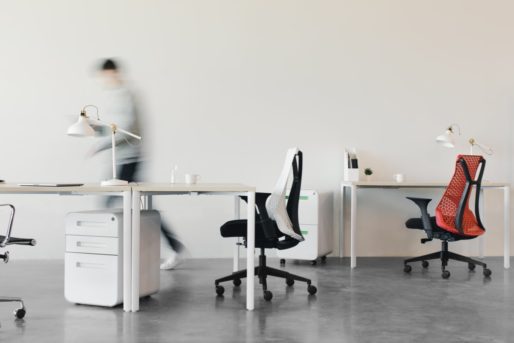 Two desks with Two Swivel Chairs and a person walking in an open office