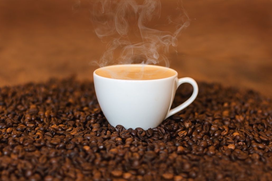 white cup of coffee with steam, sitting on coffee beans