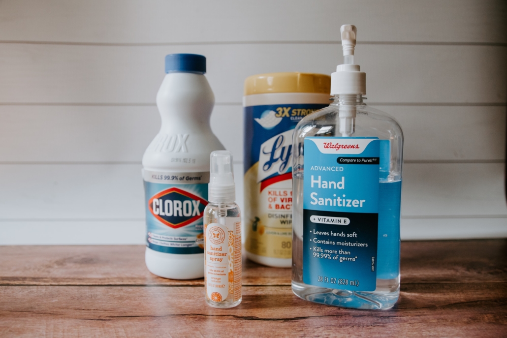 Cleaning supplies on a wooden table including bleach and hand sanitizer