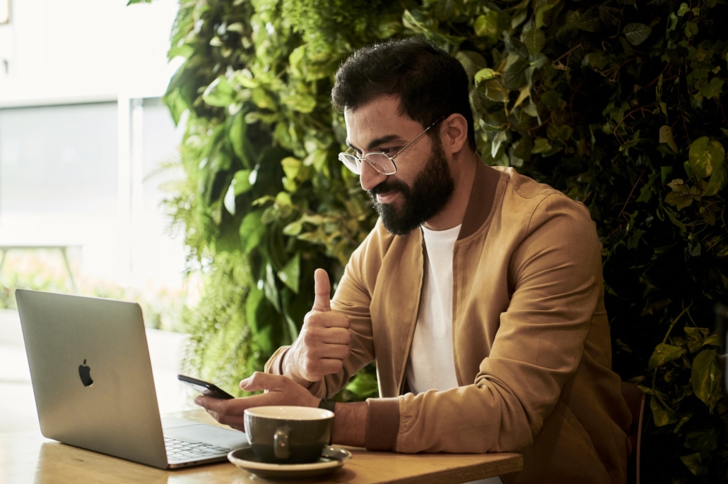 Man in glasses working from his macbook remotely giving thumbs up to the screen