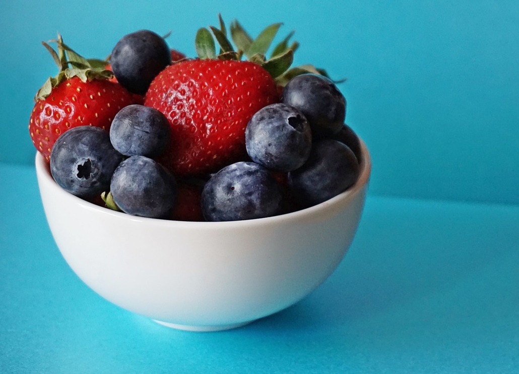 Blueberries and Strawberries in a white ceramic bowl on a blue table
