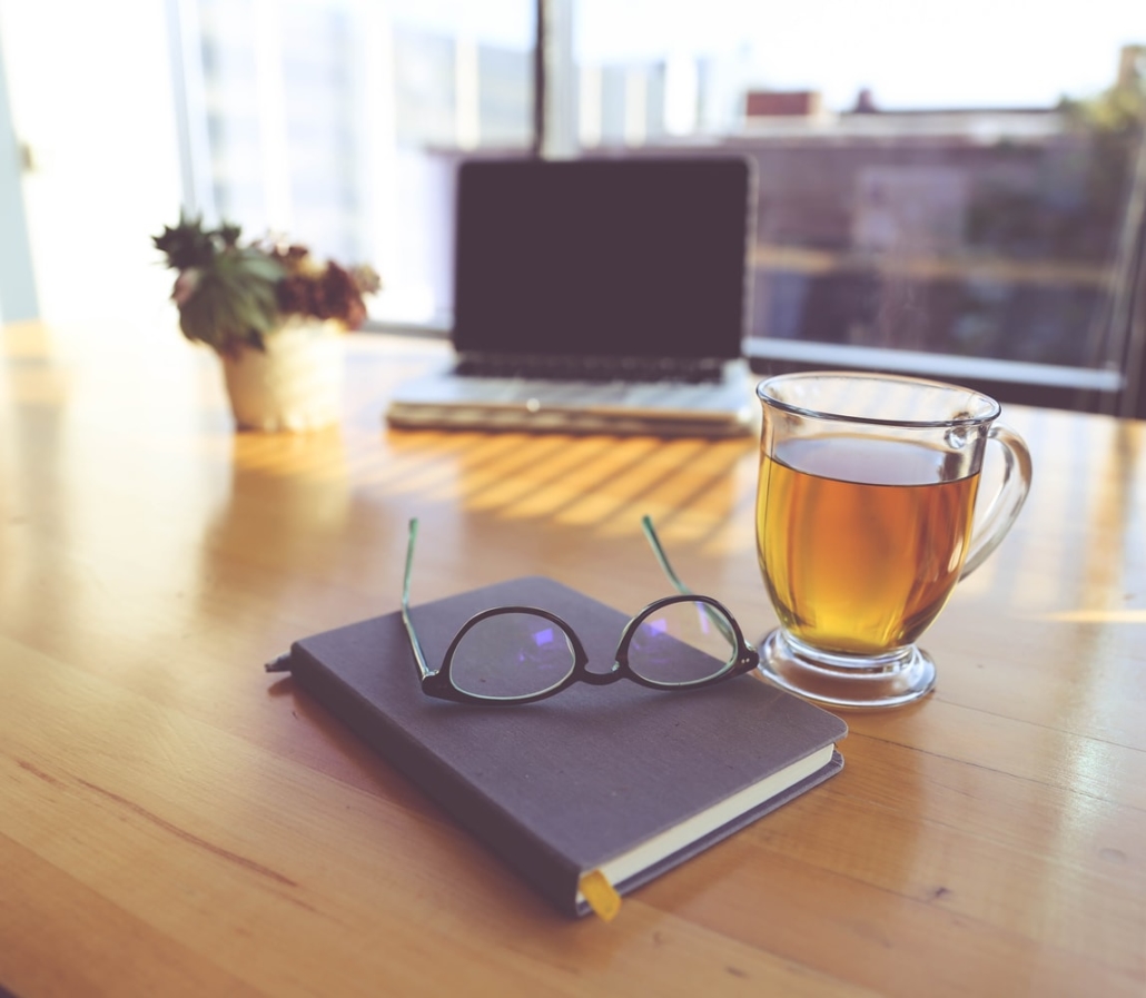 A cup of tea on someone's desk next to a pair of glasses and a notebook